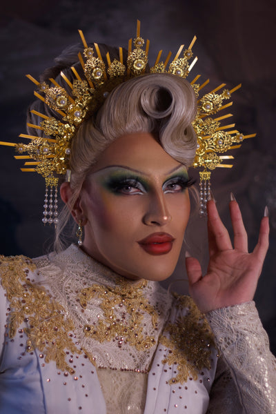 Person wearing a elaborate gold headpiece and ornate outfit with a dark background
