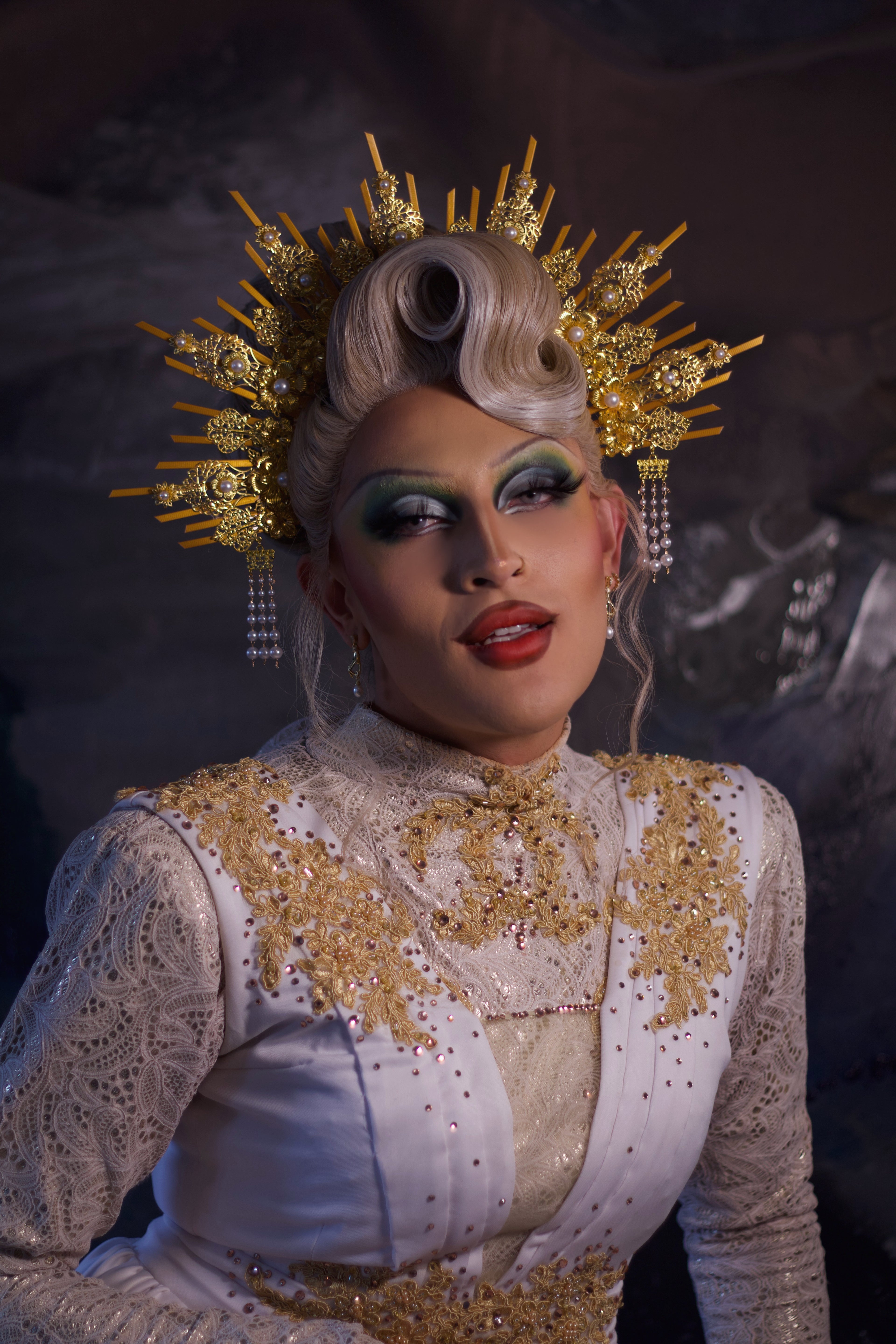Person in an elaborate costume with gold and white details against a dark background